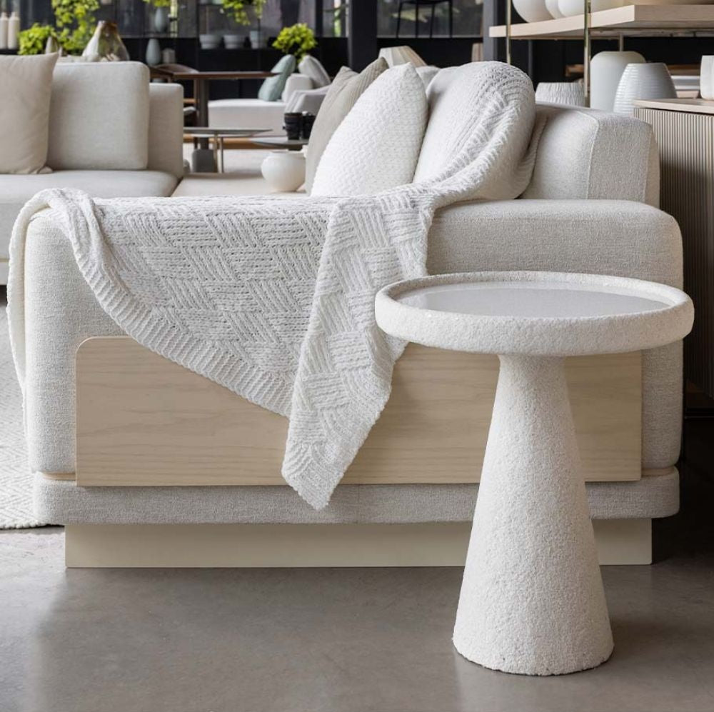 Mesa de Apoio com base cônica em concreto pintado de branco cao lado de um sofá de alto padrão.