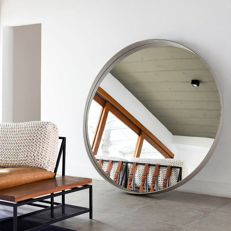 Espelho grande e redondo em um ambiente clean e minimalista, encostado na parede refletindo as costas de uma poltrona.
