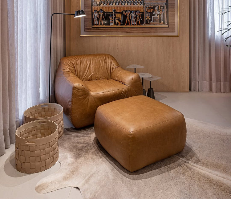 Ambiente canto de leitura de uma sala moderna com uma luminaria e com uma poltrona e um puff quadrado em couro caramelo.