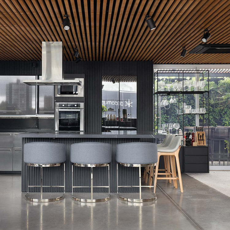 Ambiente de cozinha gourmet com balcão em éle com três banquetas com base em metal inox polido e duas com base em madeira natural