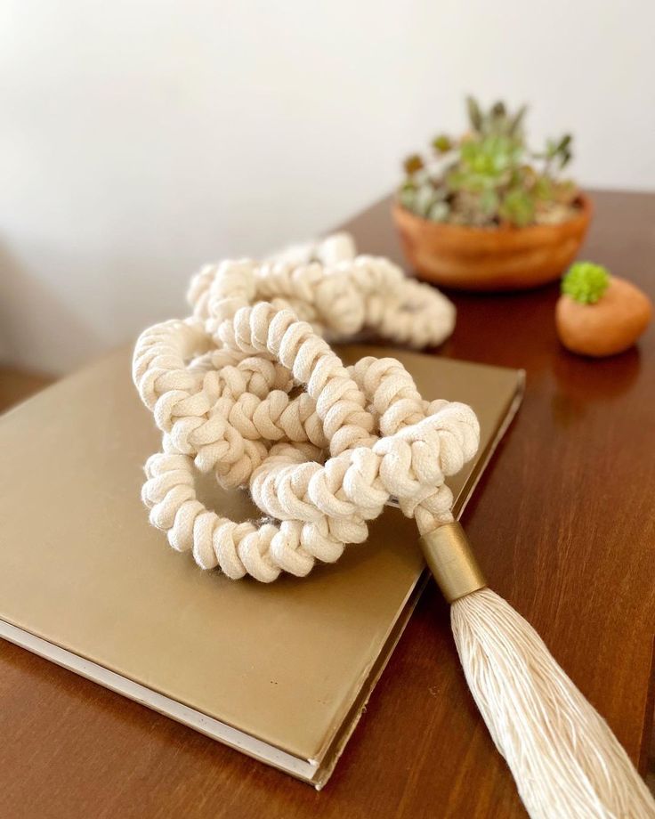 corda decorativa branca com detalhe dourado na ponta em cima de um livro que também está em cima de uma mesa de centro.