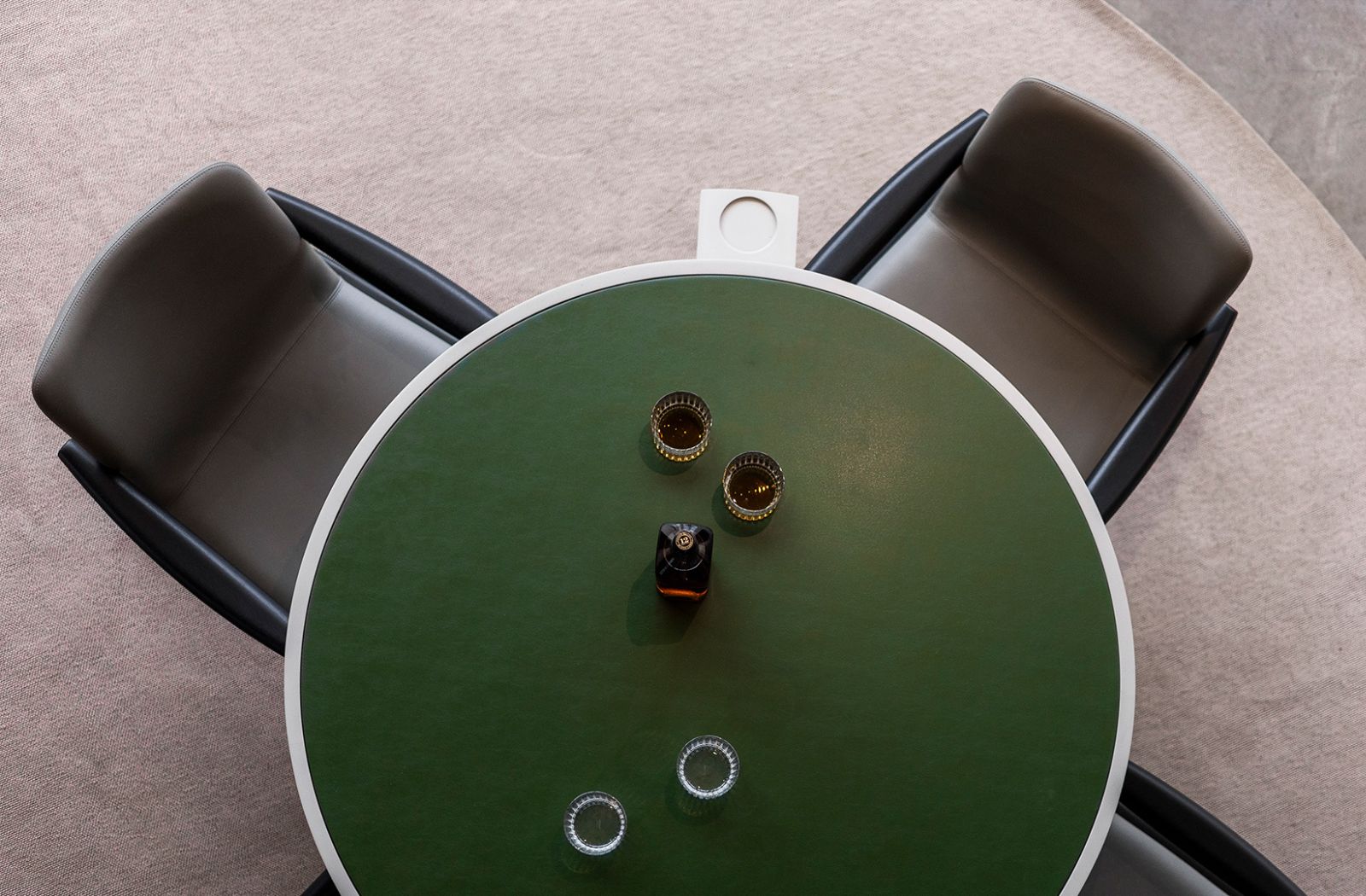 mesa redonda de quatro lugares com dois copos com wisky e dois copos com agua e no centro uma garrafa de wisky. Quatro cadeiras de alto padrao em couro e braços de madeira na cor preto.