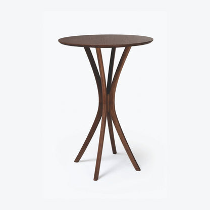 Mesa bistrô Montana em madeira tingida, com tampo redondo e base curva escultural, exibida sobre fundo branco.