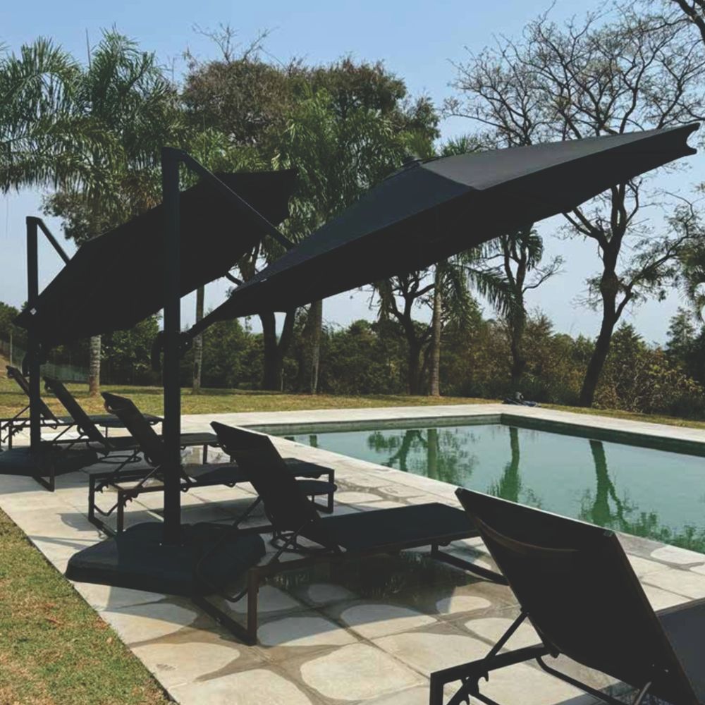 Ombrelone de centro na cor preta, com mastro e base redonda, aberto em um pátio de jardim com parede de hera.