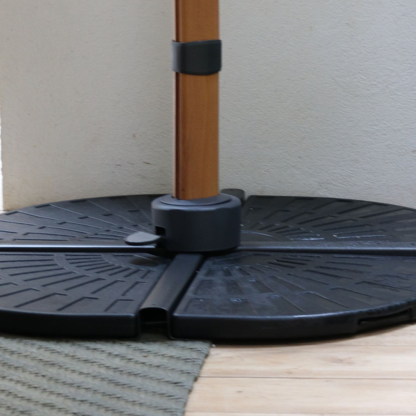 Detalhe da base de contrapeso modular do Ombrelone Manorca, mostrando a haste central encaixada no suporte de fixação preto e o pedal de giro.